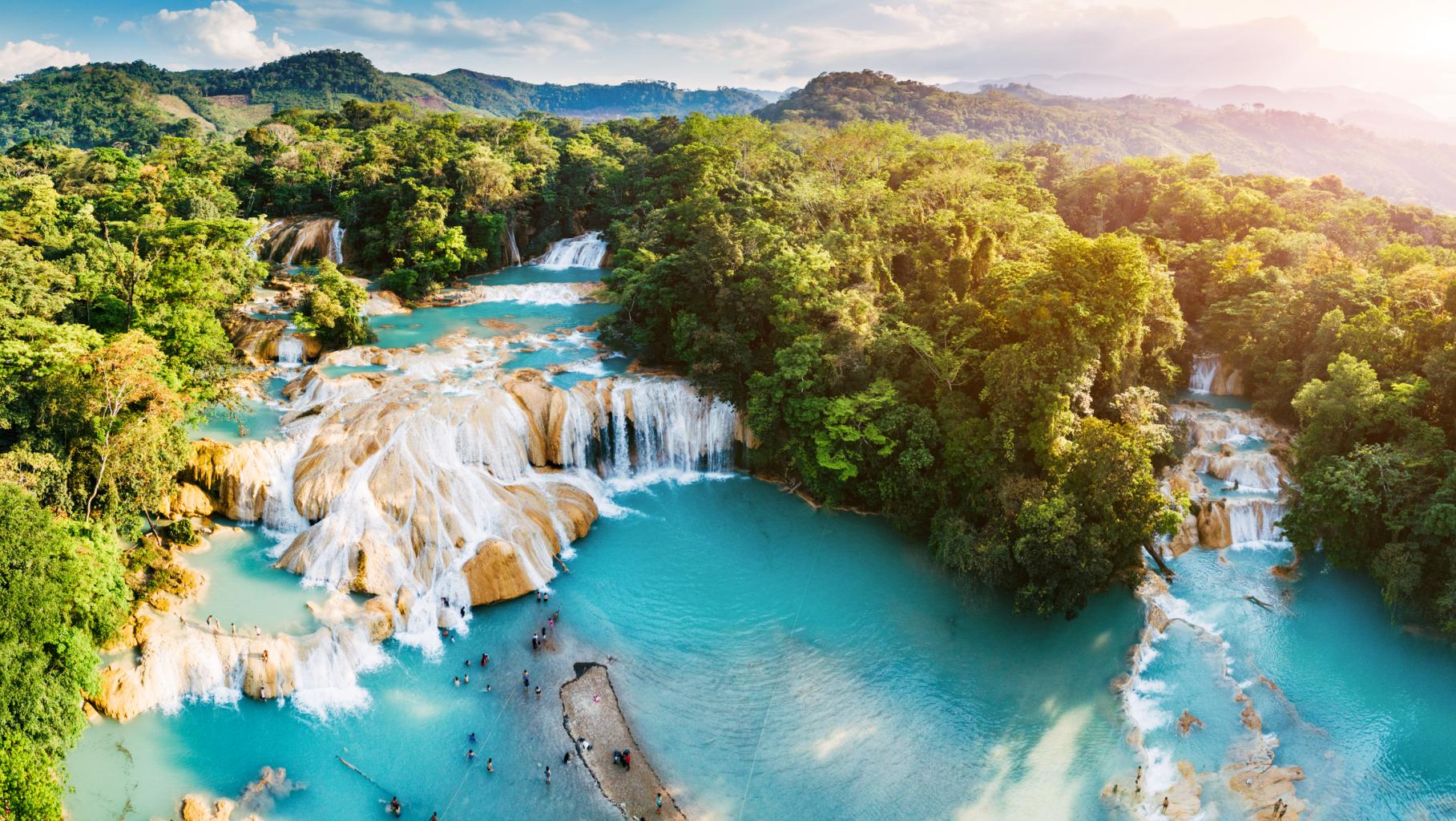 Turquoise water cascading over broad waterfalls surrounded by green forest