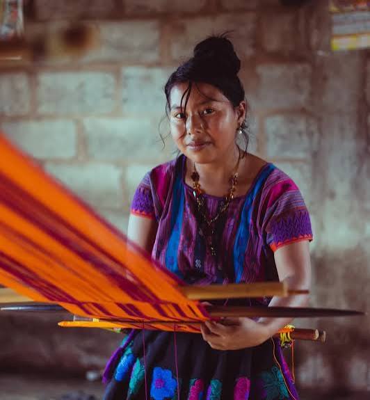 A woman weaving vivid orange and purple threads on a loom